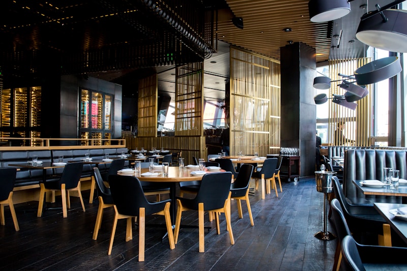 Elegantes Restaurant-Interieur mit runden Holztischen, schwarzen Stühlen und Glas-Weinkeller